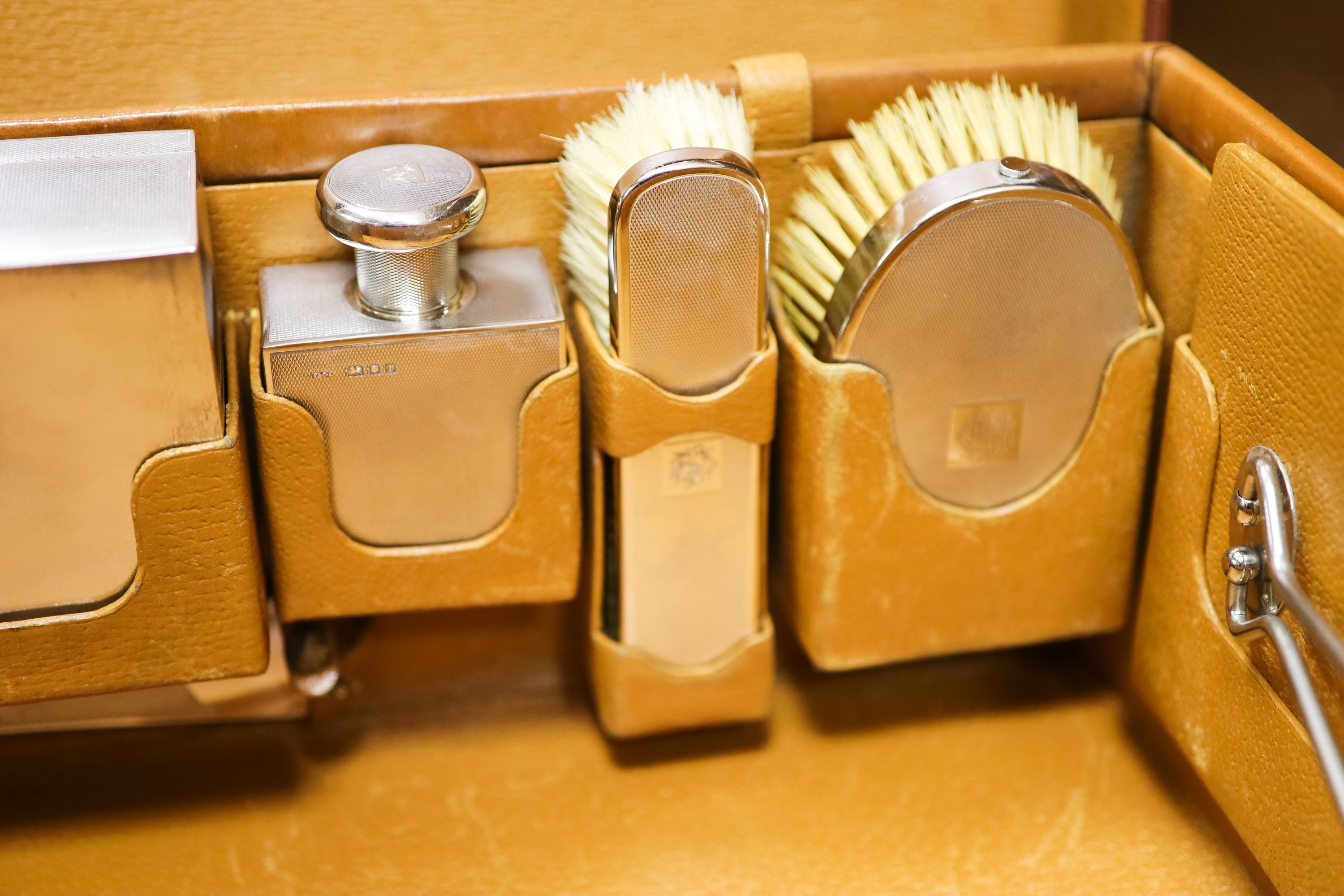 A 1930's Harrods pigskin travelling toilet case with seven engine turned silver fittings, including brushes, cigarette box and two scent bottles, F & Co Ltd, London, 1933, case 66.5cm.